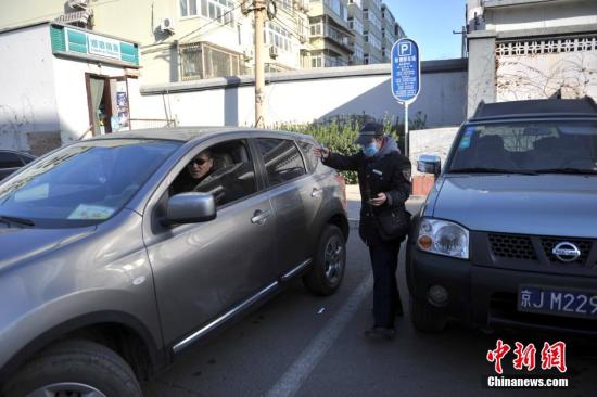 今年元月起，北京全市3000多名路側停車管理員上崗證更換，新上崗證標有二維碼，市民用手機掃描即可看到管理員的照片、姓名、所在公司、監(jiān)督電話等詳細信息。若冒用或偽造，掃描出來的信息將與實際不符，一旦遇到假收費員，市民有權拒絕交費。圖為停車場管理員張大姐為車主指揮倒車。<a target='_blank' href='http://www.chinanews.com/' >中新網(wǎng)</a>記者 金碩 攝